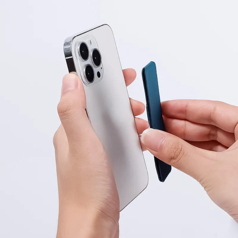 A close-up of a hand holding a silver smartphone while another hand applies a dark blue protective film or skin to the back of the phone.