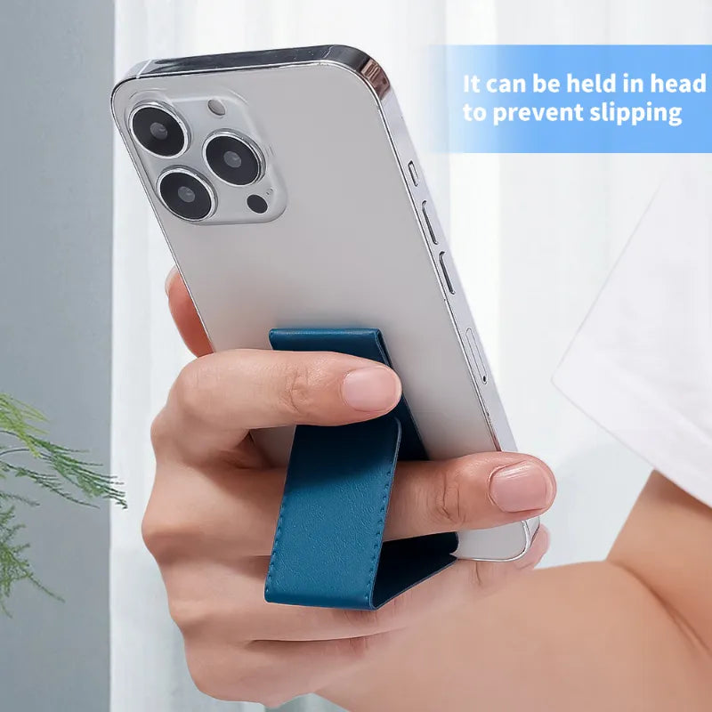 A hand holds a silver smartphone with a blue leather phone strap stand attached, shown in a bright indoor setting with a text overlay explaining its use.